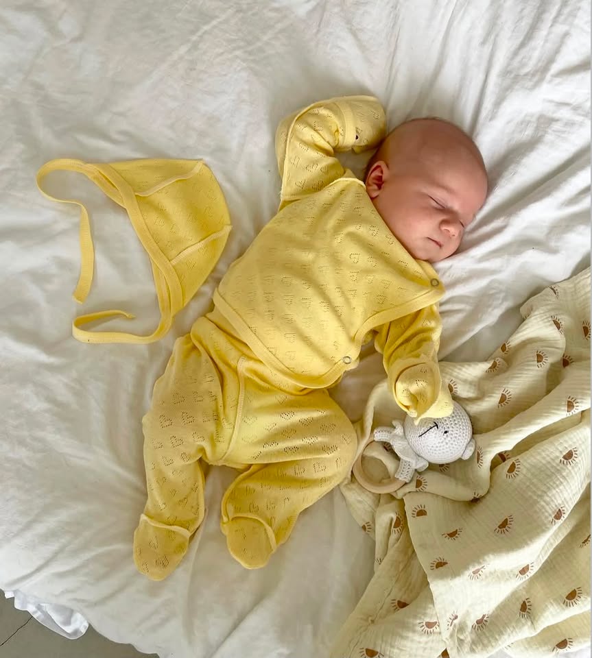 Neonato che dorme con set Liolia giallo - body, pantalone e cappellino con perforazione a cuori